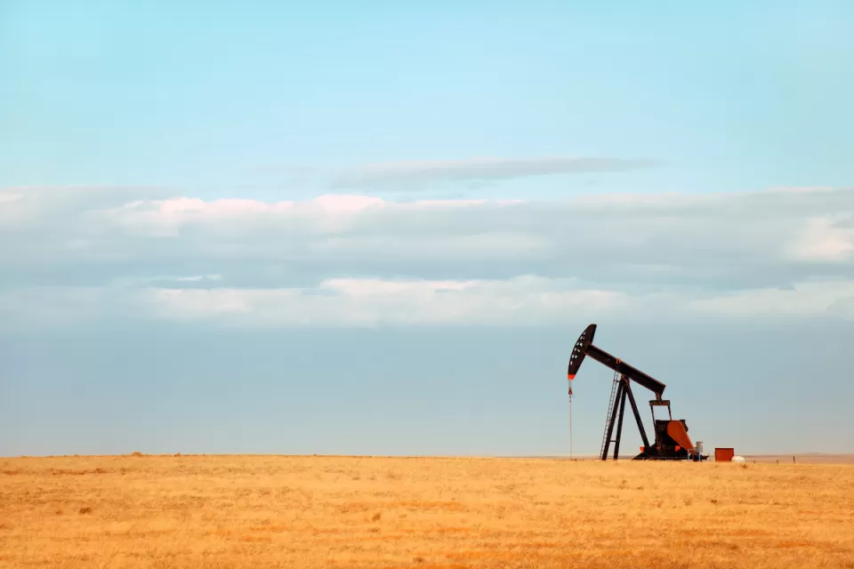 Single oil derrick on dry prairie with faded blue sky in background.